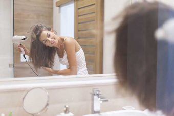 鏡の前でドライヤーで髪を乾かす女性